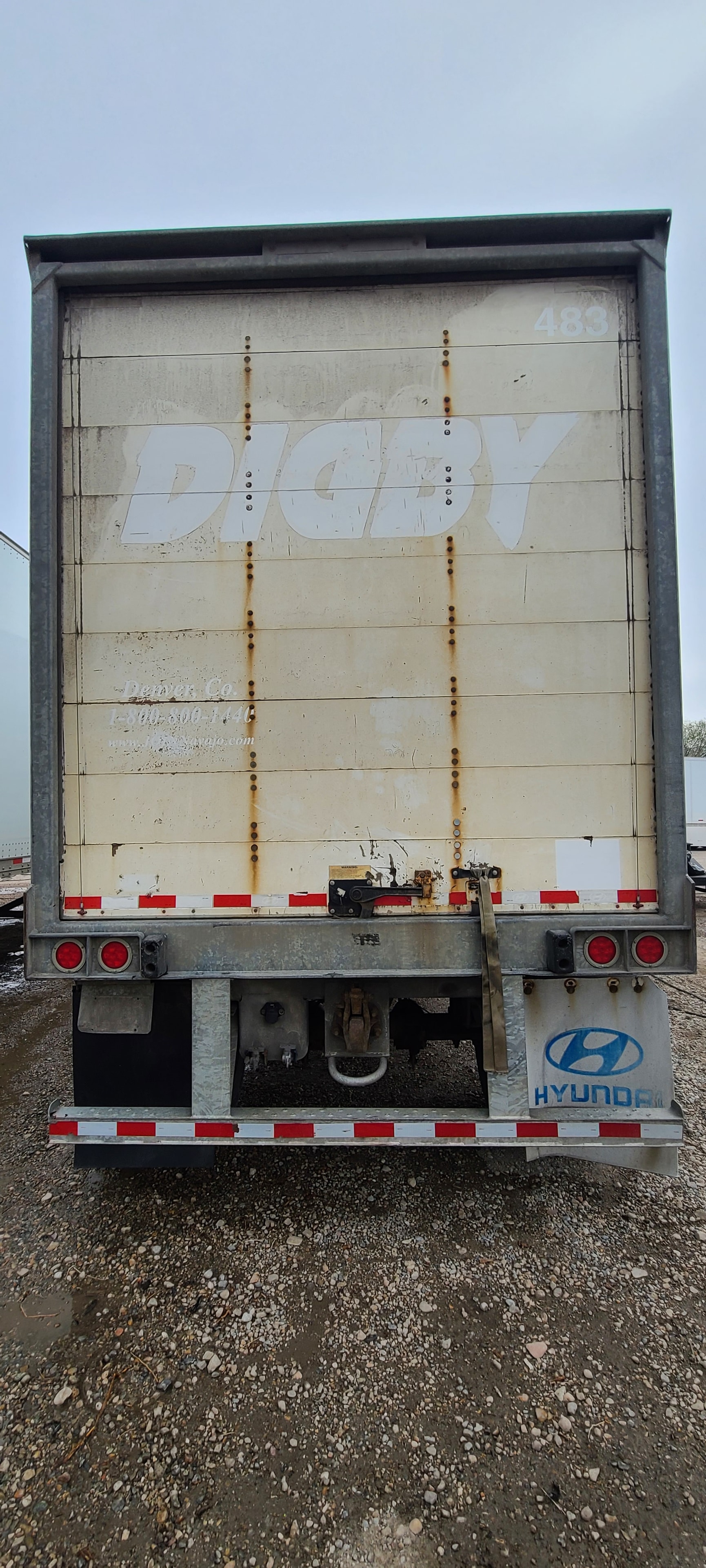 Digby pup trailer #483 rear door after decal removal — ghost lettering and adhesive residue visible before final pressure wash and surface restoration