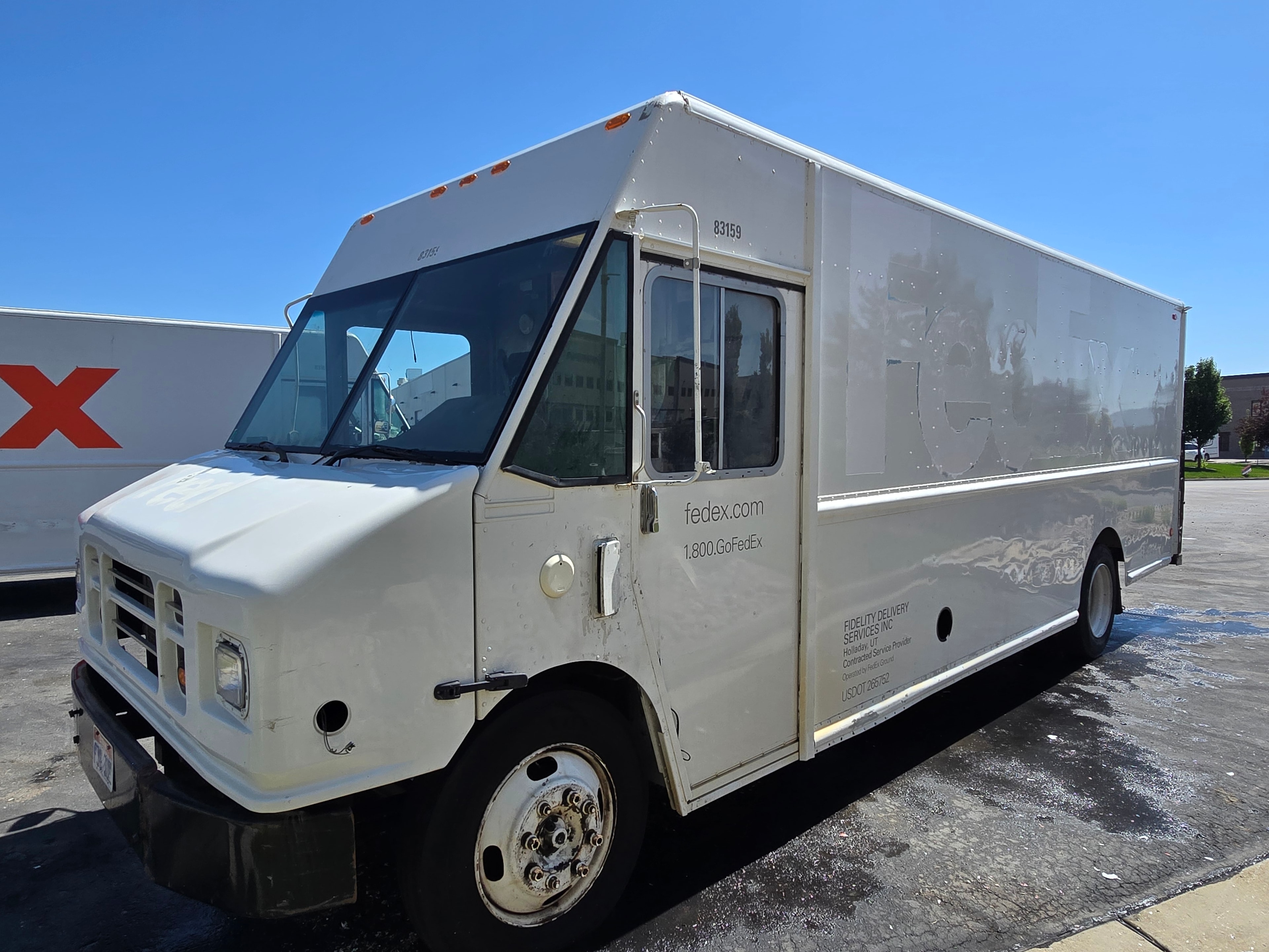 FedEx Ground step van wide side shot during decal removal — ghosting outline on panel, vehicle being pressure washed