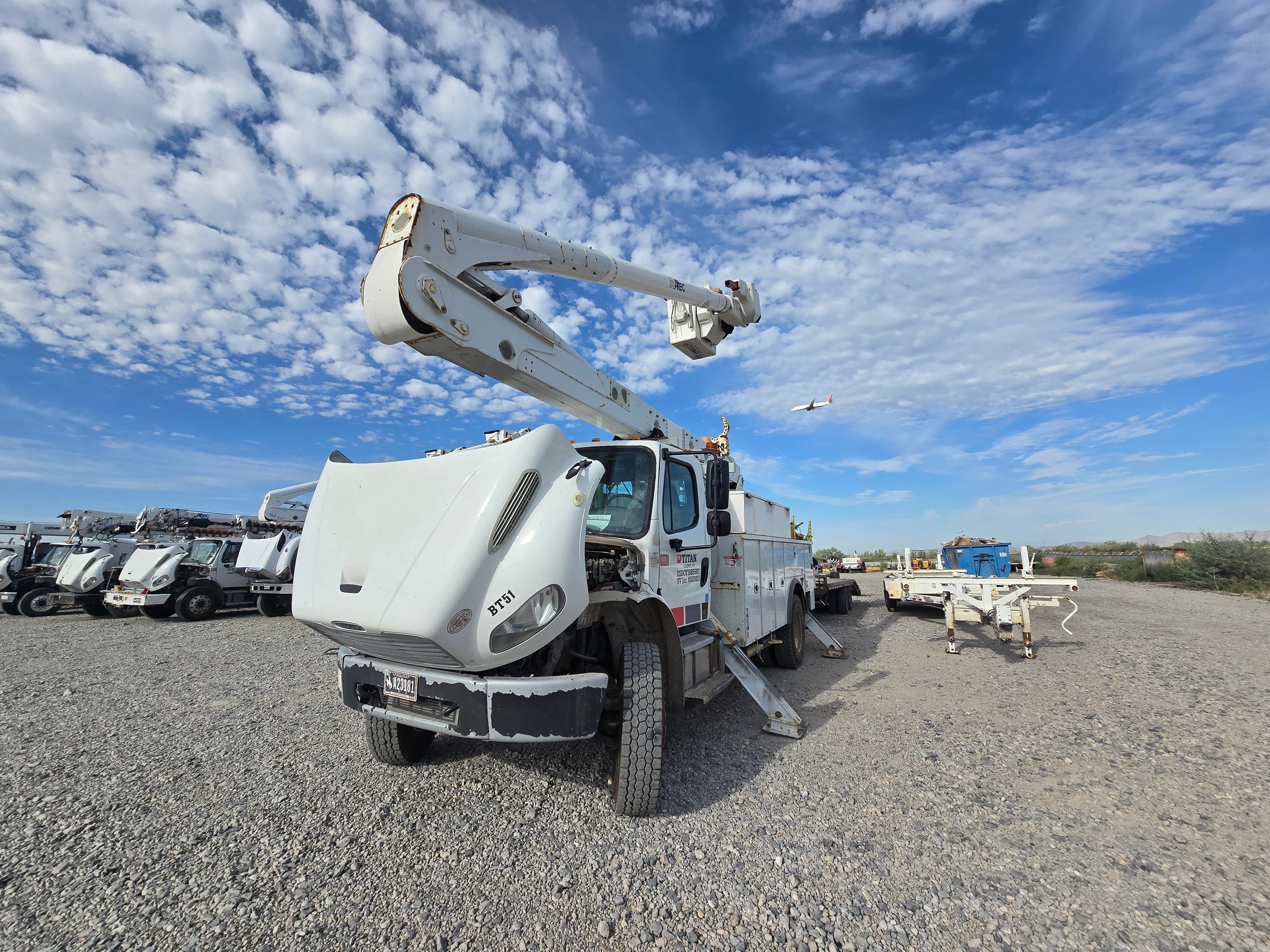Titan Freightliner bucket truck BT51 front quarter before washing — gravel lot with fleet of utility trucks