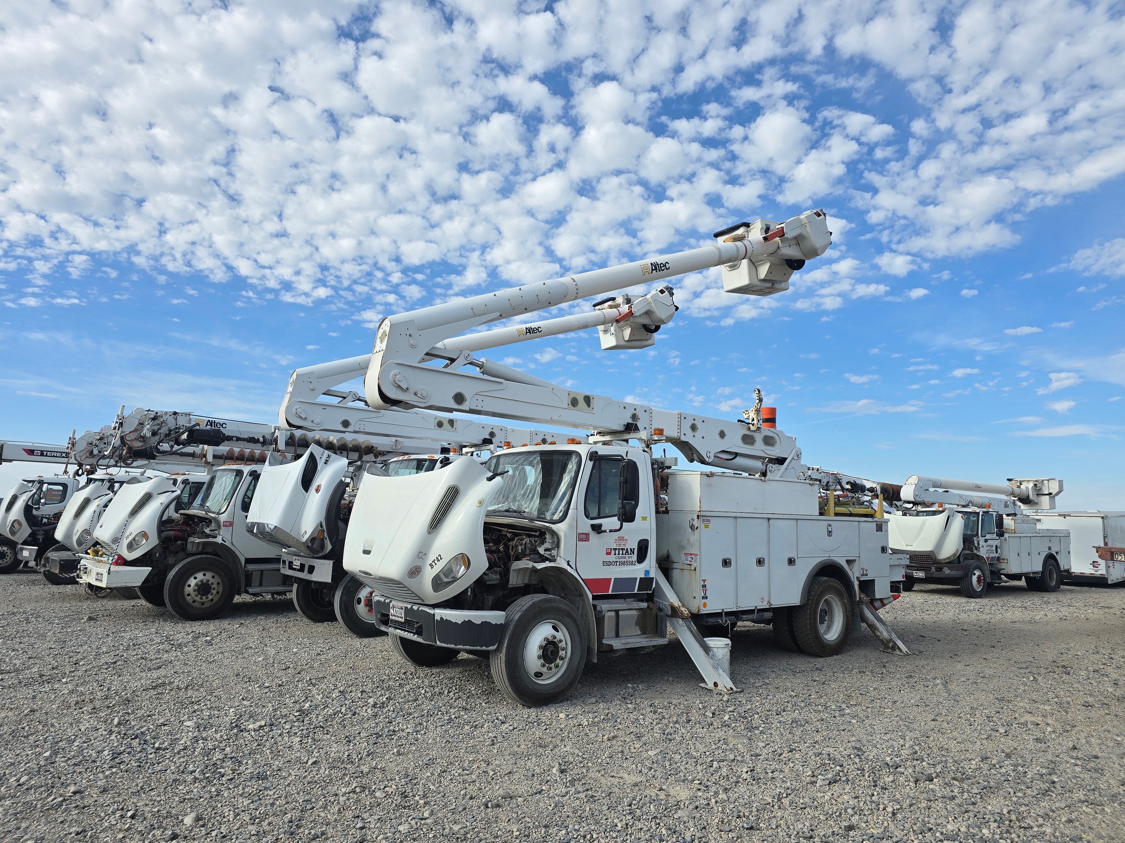 Titan Freightliner bucket truck BT42 with dual Altec booms before washing — fleet of utility trucks in gravel yard